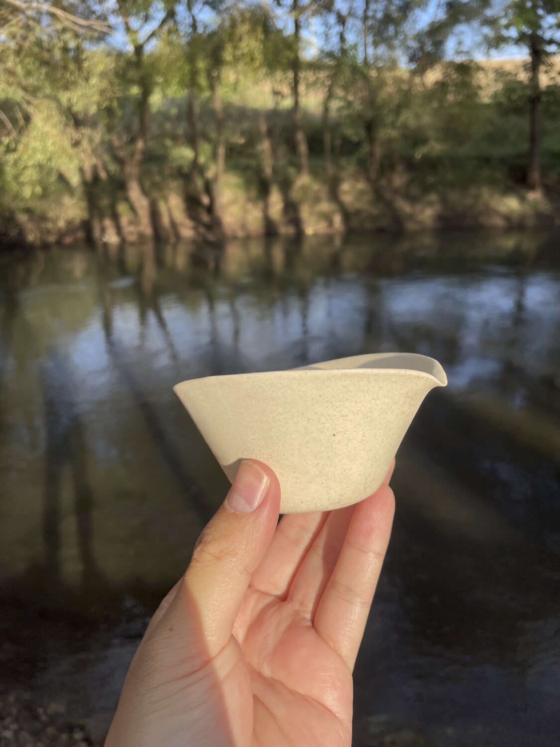 A small handmade white pouring vessel beside the water